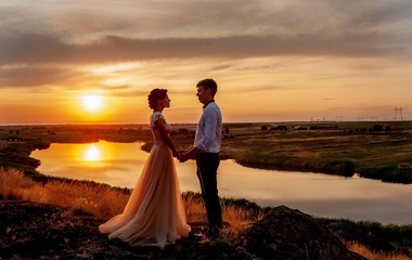 A loving couple, a guy and a girl stand and look at each other at sunset on the mountain against the background of the river. Wedding day