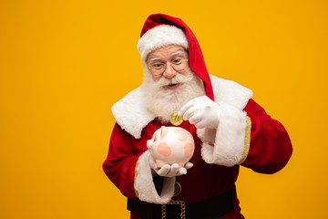 Santa Claus putting coin into a ceramic piggy bank. Savings concept for the end of the year. Spending over Christmas. Spent on Christmas presents.