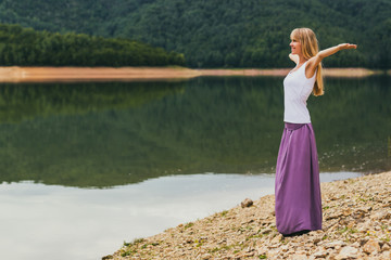 Woman with her arms outstretched enjoys spending her time by the lake.