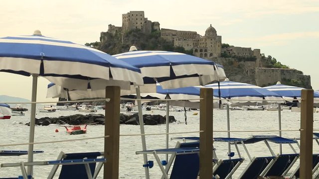 Umbrellas and deckchairs on the beach of Ischia Porto. In the background the Aragonese Castle.
