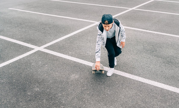 Teenager skateboarder boy with a skateboard on asphalt playground doing tricks. Youth generation Freetime spending concept image.