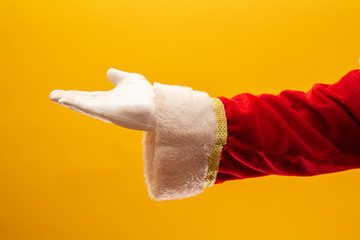 Close-up of Santa Claus gloved hand show giving gesturing on yellow background. Festive time for happy New Year, Merry Christmas, traditional seasonal celebration.