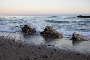 Fototapeta na wymiar Waves crashing on beach rocks sunset
