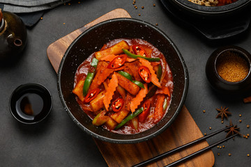 Korean Food Style : Top view of Hot and spicy Stir-fried rice cake ( Tteokbokki ) put in the black bowl or dish and placed on a wooden tray