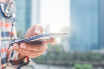 close up handsome man using hand typing smartphones and touch screen working search with app devices outdoor in city with sunrise and building background. 5G technology connecting the world.