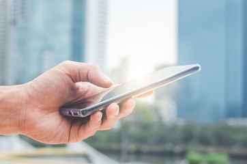 close up handsome man using hand typing smartphones and touch screen working search with app devices outdoor in city with sunrise and building background. 5G technology connecting the world.