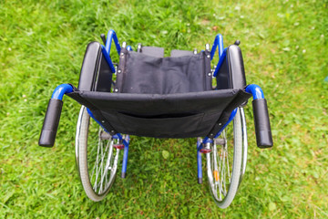 Empty wheelchair standing on grass in hospital park waiting for patient services. Invalid chair for...
