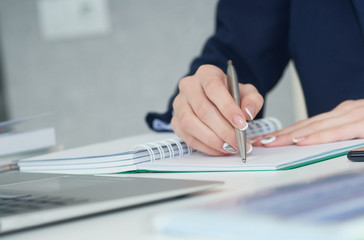 Fototapeta premium Young businesswoman writing in notepad while sitting at the office. Female hands holding a pen and making notes close up.