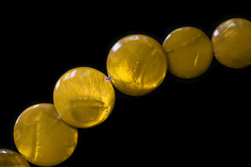 Yellow necklace made of round flat beads on a dark background close up