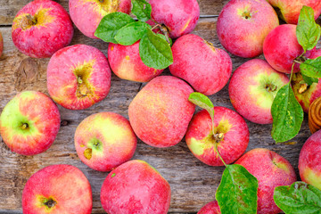 Fresh red apples with green leaves on a wooden old table.