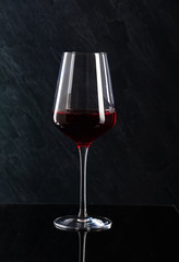 Bottle and glass of red wine on black background