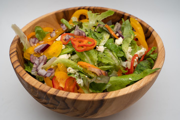 Isolated close up shot of mixed organic vegetable salad with olive oil dressing in a wooden bowl