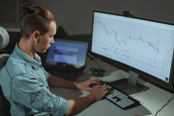 Young male programmer working late at night, copy space. Male stock trader using two computers,...