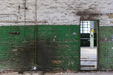 Front view of rough old scratch painted with white and green brick wall, damage electric cables and rectangular door in abandon industrial building.