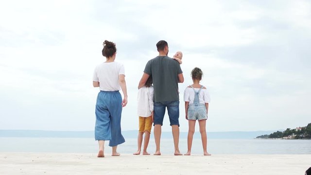 Family holidays on the Mediterranean coast. Happy family vacation. Friendly family with two children are standing on the seashore, kissing and hugging, rear view