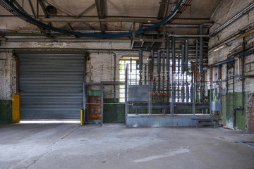 Interior view of open old dirty room with the controller zone of pressure sensors, pump station and metal pipe system on ceiling and wall in factory or industrial building.