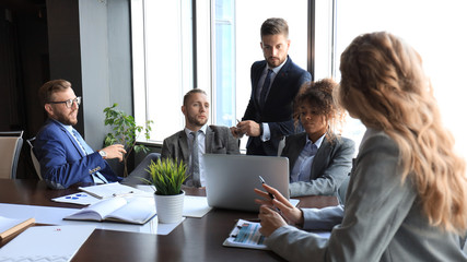 Group of modern business people in formalwear discussing business and smiling while sitting in the office