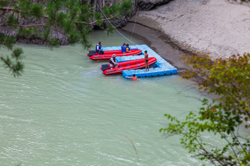View of a red rubber motor boat near a blue plastic pier on a green river in the mountains