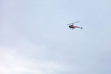 A red pleasure helicopter flies in the sky during a sightseeing walk against a gray sky. Air Transport.