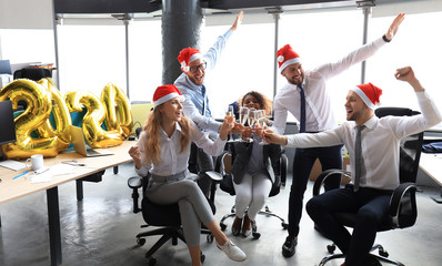 Business people are celebrating holiday in modern office drinking champagne and having fun in coworking. Merry Christmas and Happy New Year 2020.
