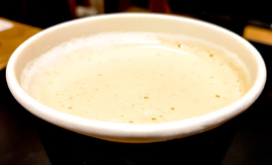 Top view close-up of a paper cup of coffee with milk and foam on a dark background of cafe interior