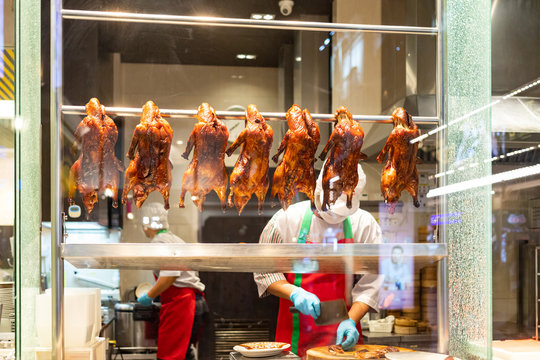 Roasted ducks hanging on rail showcase in restaurant's ketchen, Chef preparing roasted duck menu