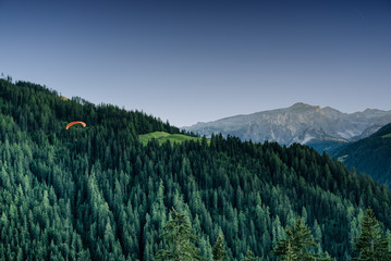 orange paraglider in Dolomite mountain landscape descending into a forest valley