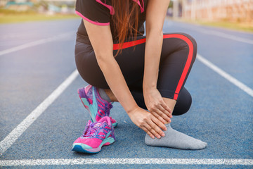 Female runner athlete ankle injury and pain. Woman suffering from painful ankle while running on the blue rubberized running track.