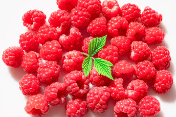 Fresh red raspberries are scattered on a white surface. A lot of berries and one leaf. View from above