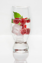 Fresh raspberries in a glass of mineral water and ice cubes on a white background. Refreshing summer drink.