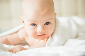Happy baby with a towel after the shower in bed at home