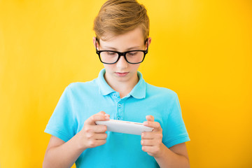 Handsome boy in glasses plays tablet. The concept of poor eyesight, harm of gadgets, myopia