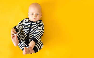 Calm curious baby lying on yellow background, looking at camera, top view, copy space