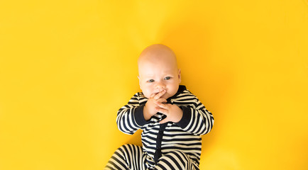 Calm curious baby lying on yellow background, looking at camera, top view
