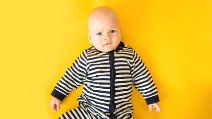 Calm curious baby lying on yellow background, looking at camera, top view
