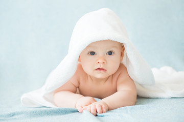Happy baby with a towel after the shower in bed at home