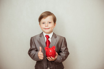 Happy child boy stands in a fashionable suit with a piggy Bank in his hands. Success, creative and innovation business concept