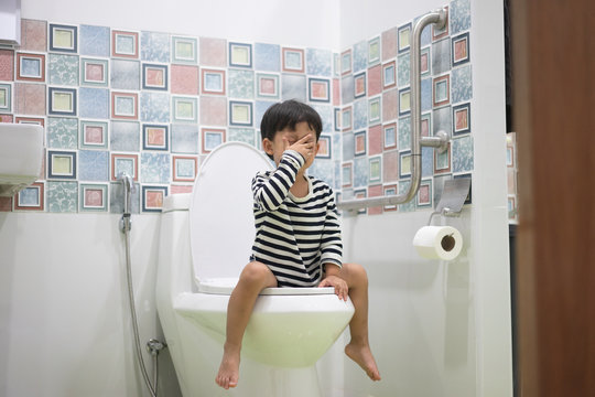 A kid is sitting on toilet with suffering from constipation or hemorrhoid.