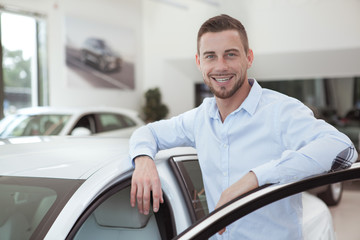 Naklejka na ściany i meble Handsome young man buying a new car at dealership salon