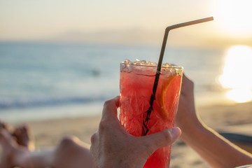 A person is holding a red cocktail at the beach.Vacations concept.