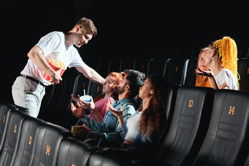 drunk man holding popcorn and flirting with ginger girl at the cinema. side view photo