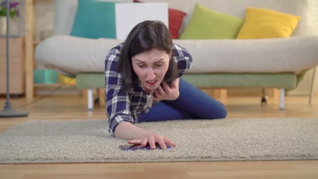 A young woman in a shirt had a heart attack and she tries to reach the smartphone lying on the floor