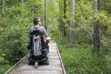 Happy man on wheelchair in nature. Exploring forest wilderness on an accessible dirt path.