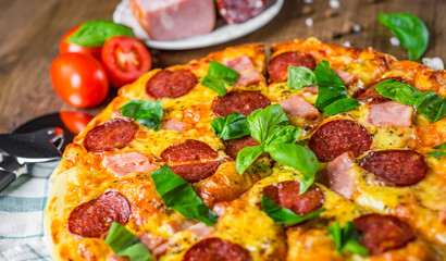 Pepperoni Pizza with Mozzarella cheese, salami, ham, Spices and Fresh basil. Italian pizza on wooden table background