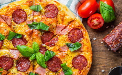 Pepperoni Pizza with Mozzarella cheese, salami, ham, Spices and Fresh basil. Italian pizza on wooden table background