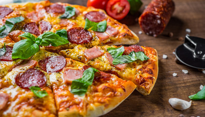 Pepperoni Pizza with Mozzarella cheese, salami, ham, Spices and Fresh basil. Italian pizza on wooden table background