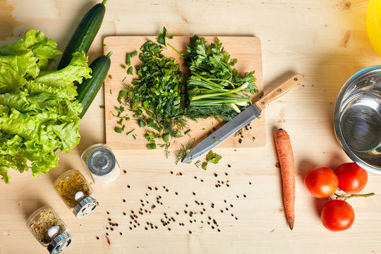 Top view of wooden table with fresh raw cucumbers, lettuce, carrots, tomatoes, spices and chopped scallions on it, ingridients for cooking healthy and tasty meal. Culinary concept.