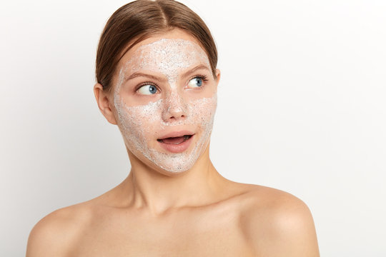 happy young woman with white facial mask, with nacked shoulders, takes care of her beauty and appearance, wears white towel on body, isolated over white background.sale, discount in beauty salon