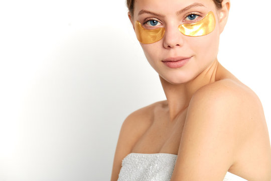 young woman with yellow mask under eyes wearing towel on her nacked body looking at the camera. Fresh Facial Skin. health, face, skin care, isolated white background, studio shot