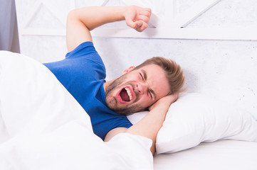 Comfortable place to pass out. Sexy man lying in comfortable bed. Handsome guy yawning and feeling comfortable after waking up in morning. Making more comfortable by lying